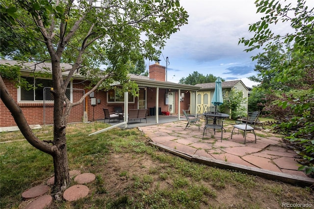 6077 Flower St, Arvada, CO 80004 - rear view of house with a patio, brick siding, and a chimney
