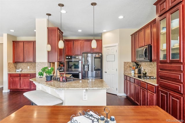 14119 W 89th Loop, Arvada, CO 80005 - kitchen featuring appliances with stainless steel finishes, reddish brown cabinets, dark wood-style floors, a center island with sink, and recessed lighting