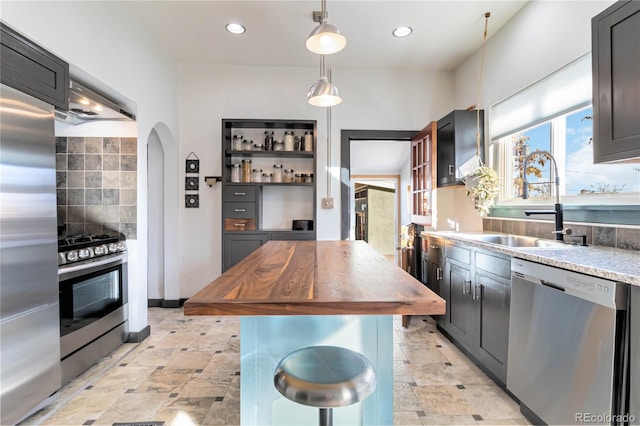 kitchen with arched walkways, butcher block counters, backsplash, appliances with stainless steel finishes, and a sink