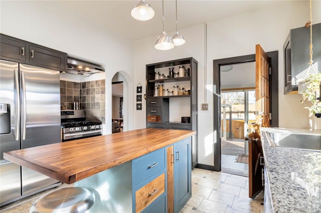 kitchen with arched walkways, a kitchen breakfast bar, stainless steel appliances, wooden counters, and a sink