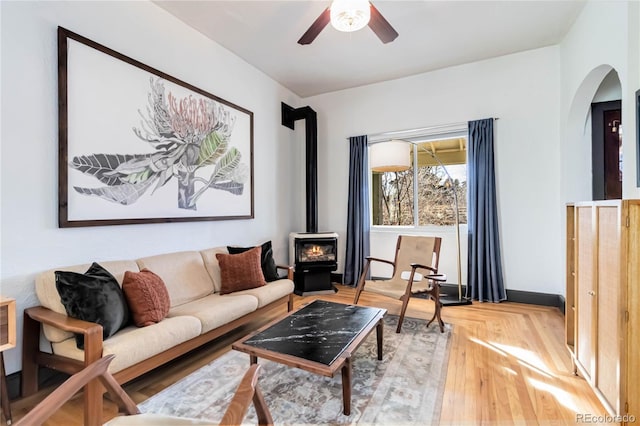 living room with arched walkways, wood finished floors, a wood stove, and a ceiling fan