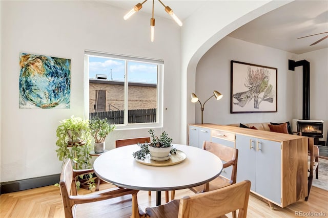 dining space featuring arched walkways, a wood stove, ceiling fan, and baseboards