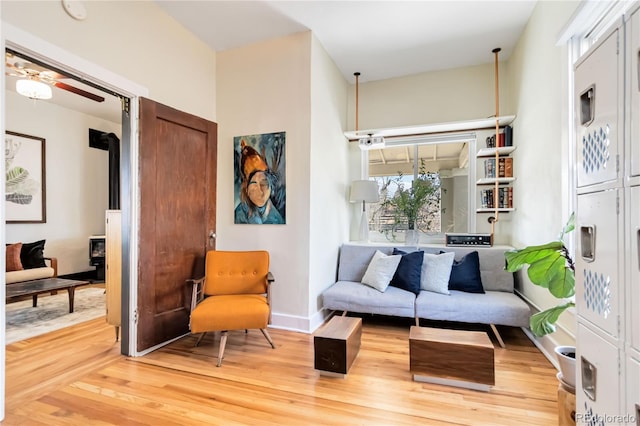 sitting room featuring a wood stove, baseboards, a ceiling fan, and wood finished floors