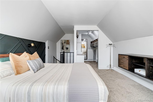 carpeted bedroom with ensuite bath, a spacious closet, baseboards, and vaulted ceiling