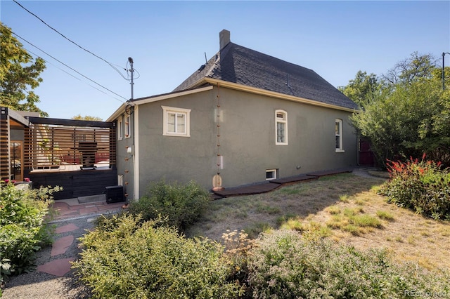 view of home's exterior with roof with shingles, a chimney, and stucco siding