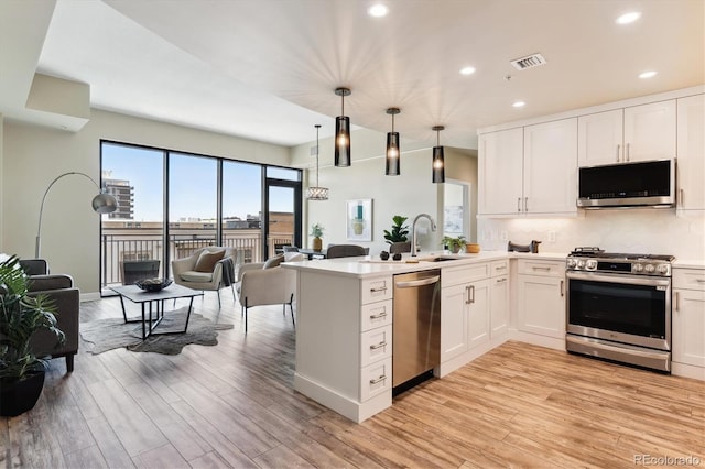 kitchen with appliances with stainless steel finishes, sink, decorative light fixtures, light hardwood / wood-style flooring, and white cabinetry