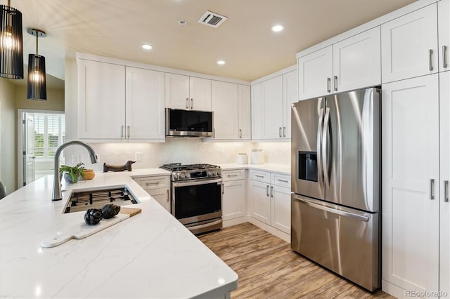 kitchen with sink, white cabinetry, light stone counters, appliances with stainless steel finishes, and pendant lighting