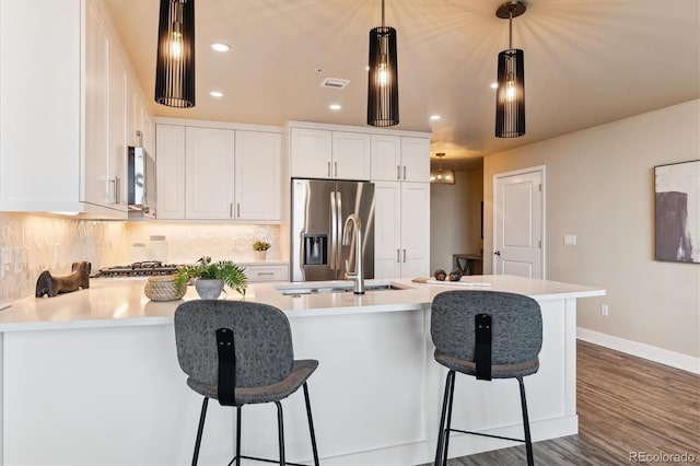 kitchen with sink, white cabinetry, tasteful backsplash, decorative light fixtures, and stainless steel fridge