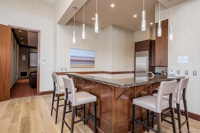 kitchen with built in fridge, pendant lighting, a kitchen bar, and light hardwood / wood-style flooring