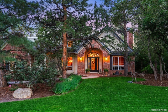 view of front of property featuring brick siding, a chimney, and a front yard