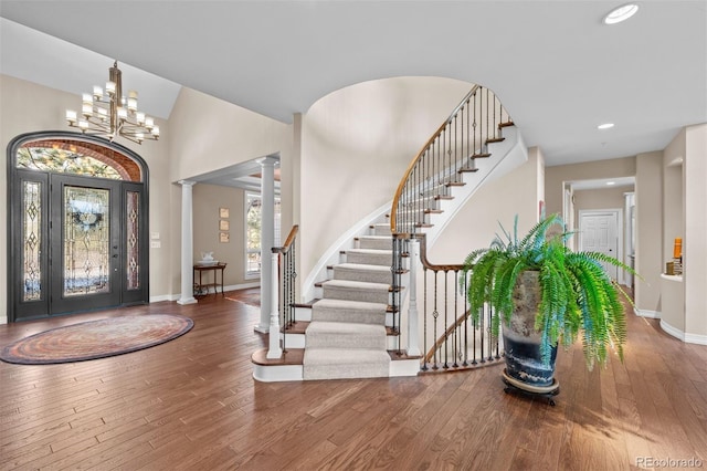 entryway with a chandelier, wood finished floors, baseboards, stairs, and ornate columns