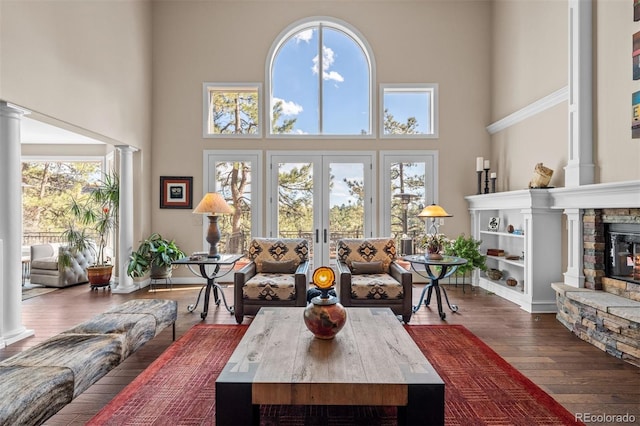 living room featuring wood-type flooring, a fireplace, decorative columns, and french doors