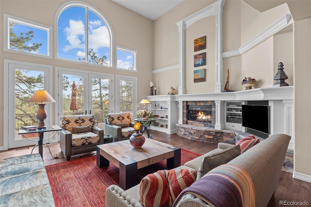 living room featuring a fireplace, wood finished floors, a towering ceiling, baseboards, and french doors