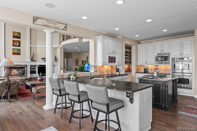 kitchen featuring a fireplace, appliances with stainless steel finishes, dark wood-type flooring, a sink, and ornate columns