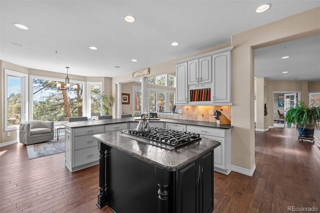 kitchen featuring a kitchen island, dark wood finished floors, stainless steel gas stovetop, and a peninsula