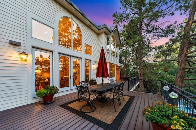 deck at dusk with outdoor dining space and french doors