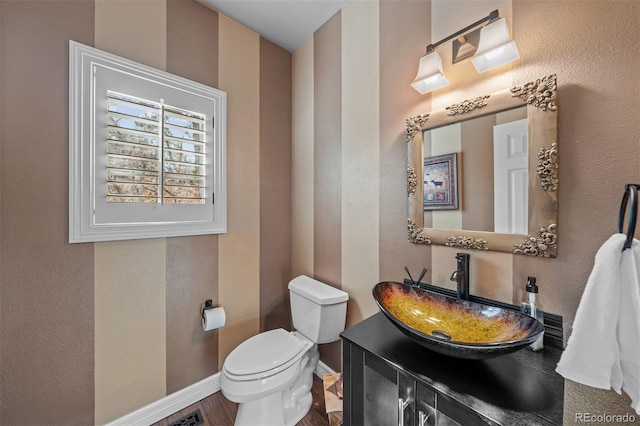 half bath featuring toilet, a textured wall, baseboards, and vanity