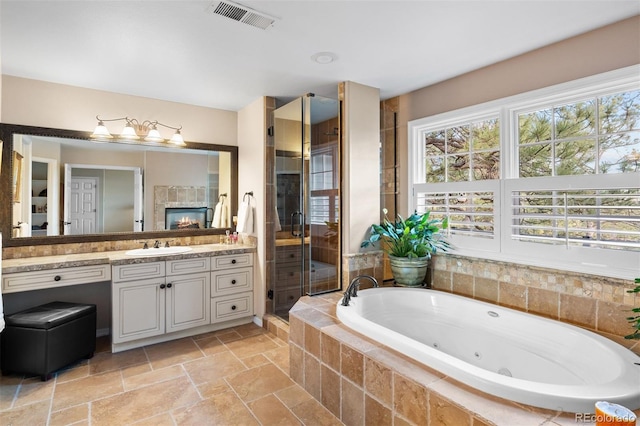 full bath featuring stone tile floors, vanity, visible vents, a tub with jets, and a stall shower