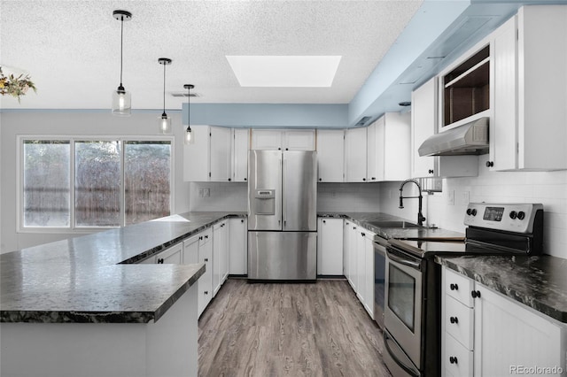 kitchen featuring kitchen peninsula, sink, a skylight, appliances with stainless steel finishes, and white cabinetry