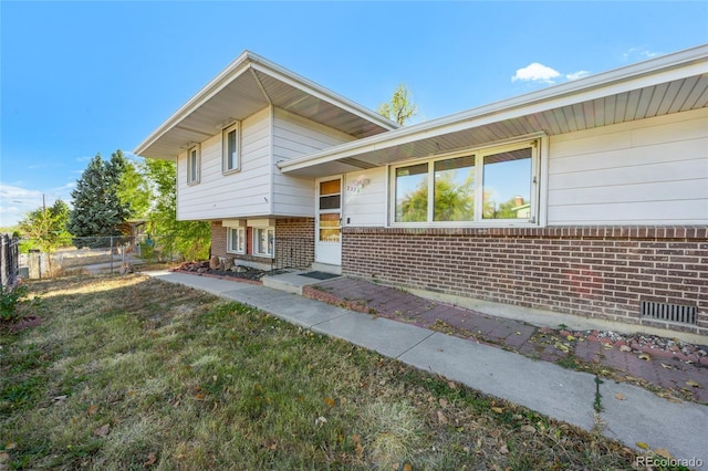 view of front facade with brick siding, a front yard, and fence