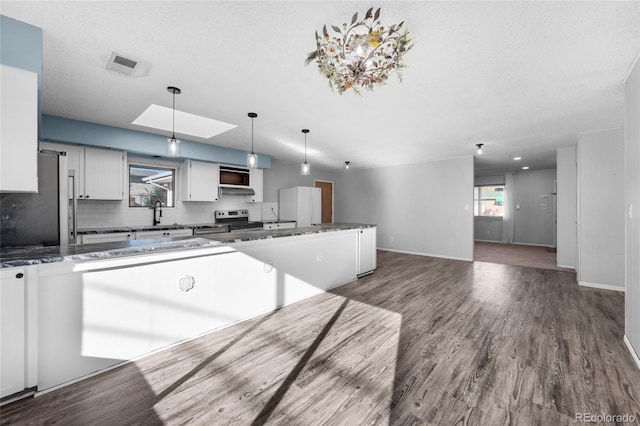 kitchen featuring dark countertops, hanging light fixtures, appliances with stainless steel finishes, dark wood-type flooring, and white cabinetry