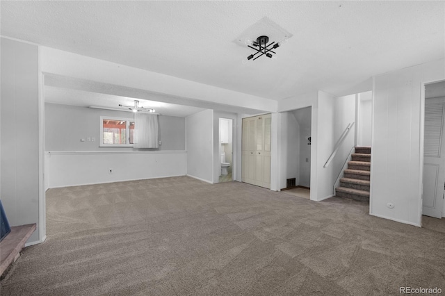 unfurnished living room featuring a textured ceiling, stairway, and light colored carpet
