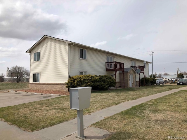 view of side of property with a balcony, a yard, and brick siding