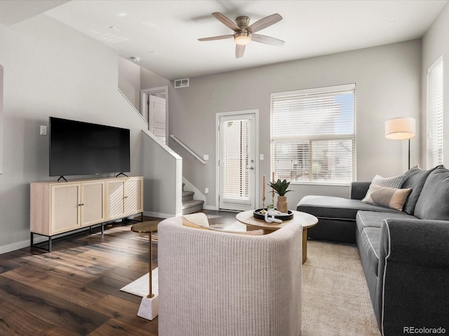 living area with visible vents, baseboards, stairway, wood finished floors, and a ceiling fan