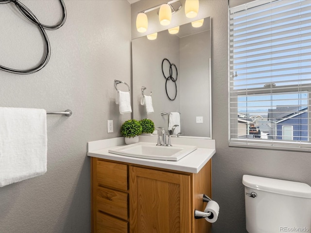 bathroom with toilet, vanity, and a textured wall