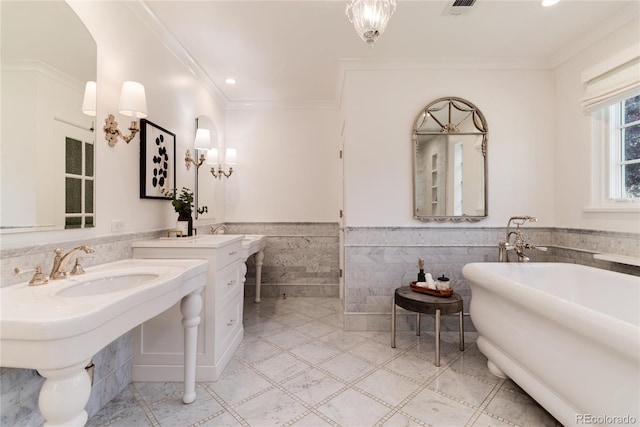 bathroom with visible vents, two sinks, a wainscoted wall, a freestanding bath, and tile walls