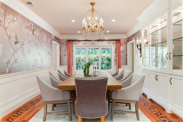 dining room with a wainscoted wall, visible vents, ornamental molding, light wood-type flooring, and wallpapered walls