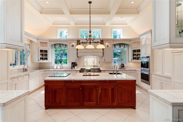 kitchen with a kitchen island with sink, glass insert cabinets, light countertops, and decorative light fixtures