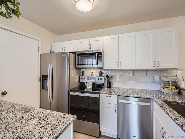 kitchen with white cabinets, appliances with stainless steel finishes, light wood-type flooring, and light stone countertops