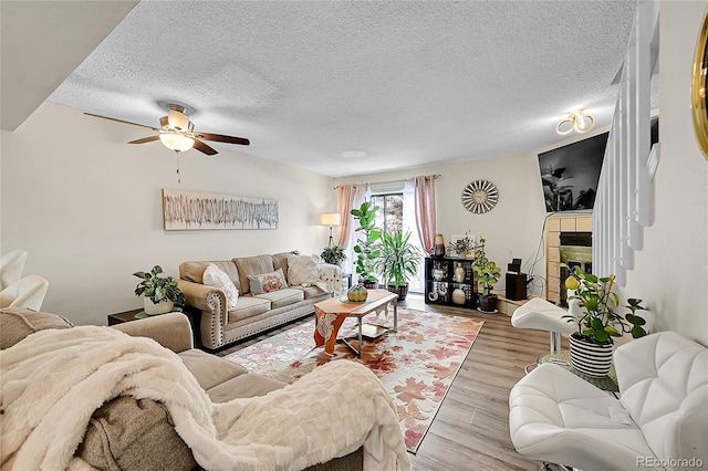 living room featuring ceiling fan, a textured ceiling, and light wood-type flooring