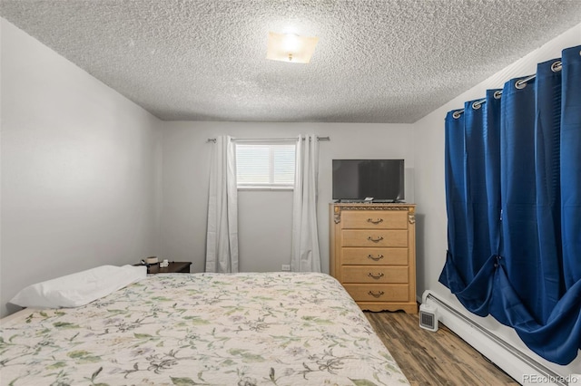 bedroom with dark wood-type flooring, a baseboard radiator, and a textured ceiling