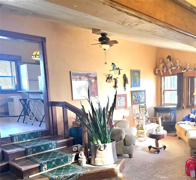 living room with ceiling fan, a wood stove, and a healthy amount of sunlight