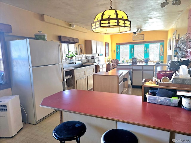 kitchen with light brown cabinetry, ceiling fan, a kitchen island, white fridge, and pendant lighting