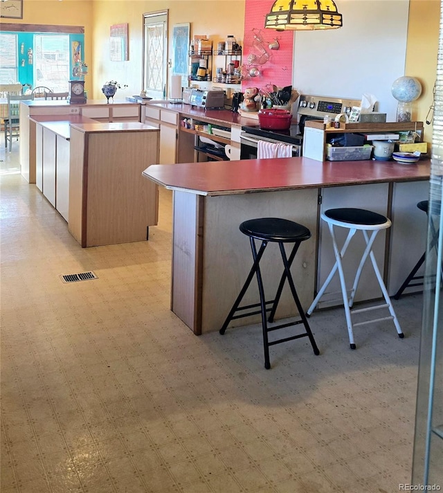 kitchen with kitchen peninsula, stainless steel range with electric cooktop, a kitchen breakfast bar, and a center island