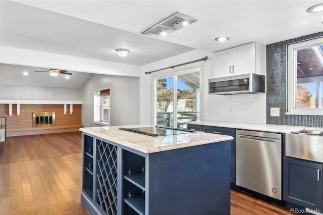 kitchen with appliances with stainless steel finishes, dark hardwood / wood-style flooring, vaulted ceiling, blue cabinetry, and a center island