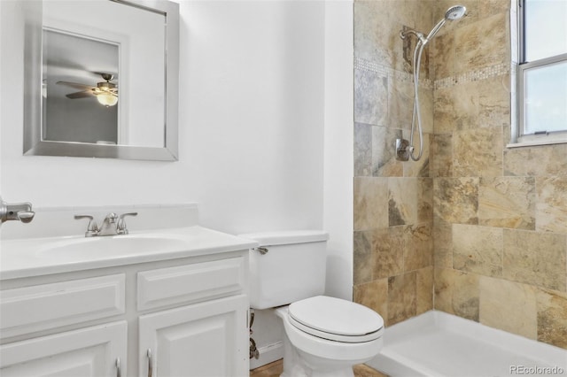 bathroom with tiled shower, ceiling fan, vanity, and toilet