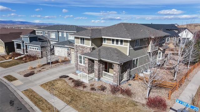 view of front of property with a shingled roof, concrete driveway, stone siding, a residential view, and a porch