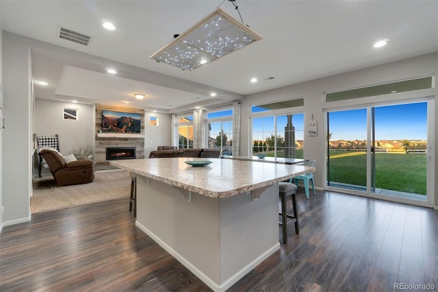 kitchen with dark hardwood / wood-style floors, a kitchen breakfast bar, a large fireplace, and a spacious island