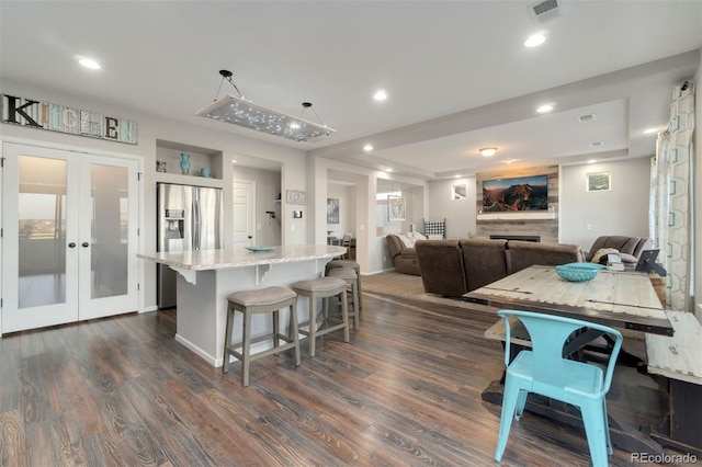 kitchen with a center island, light stone counters, stainless steel fridge with ice dispenser, dark wood-type flooring, and french doors