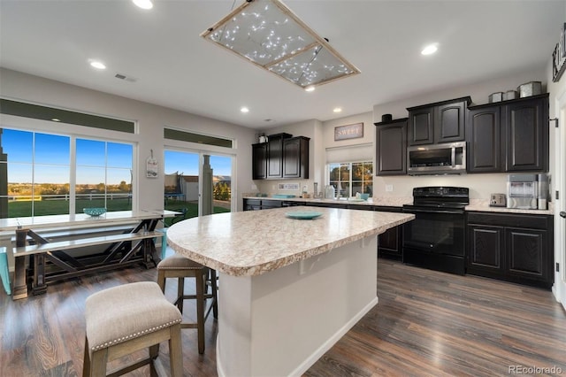 kitchen featuring dark hardwood / wood-style flooring, black range with electric cooktop, a breakfast bar area, and a center island