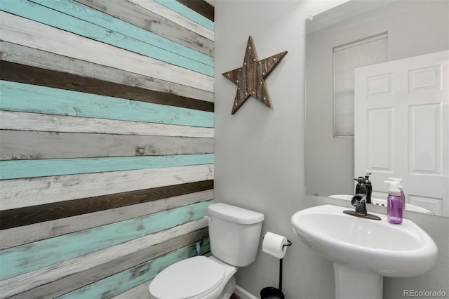 bathroom featuring sink, wooden walls, and toilet