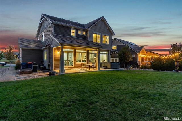 back house at dusk with a yard, a hot tub, and a patio