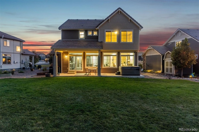 back house at dusk with a hot tub, a patio, and a lawn