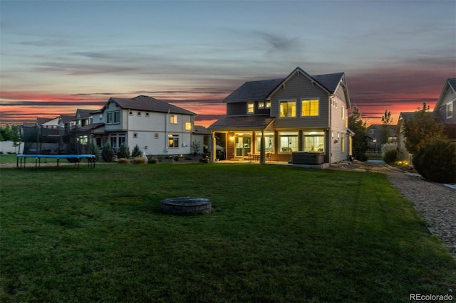 back house at dusk with a trampoline, a fire pit, a lawn, and a patio