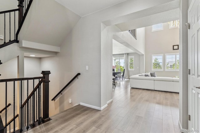 hall with baseboards, an upstairs landing, wood finished floors, and a towering ceiling