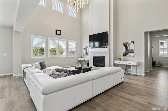 living area with baseboards, light wood-type flooring, a towering ceiling, and a tile fireplace